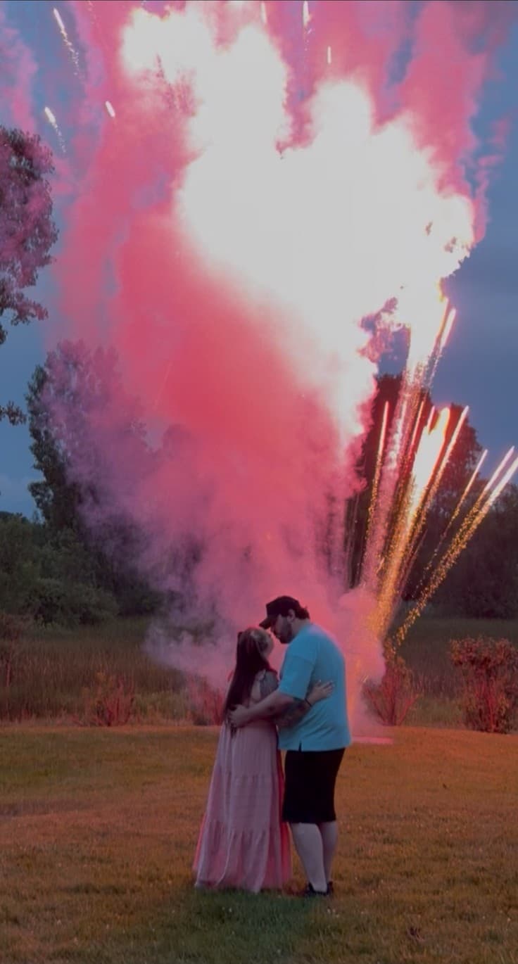 Taylor and Kevin embrace in a field at dusk as pink smoke and fireworks burst behind them, revealing that baby Gianna is a girl.